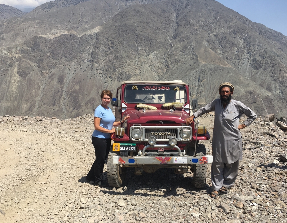 Deux personnes posant devant un vieux véhicule avec des montagnes en arrière-plan.