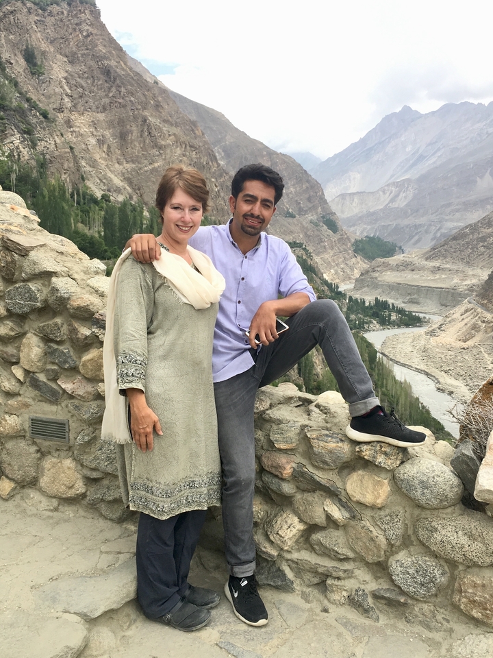 Deux personnes posant sur un mur de pierre avec une rivière et une vallée en arrière-plan.