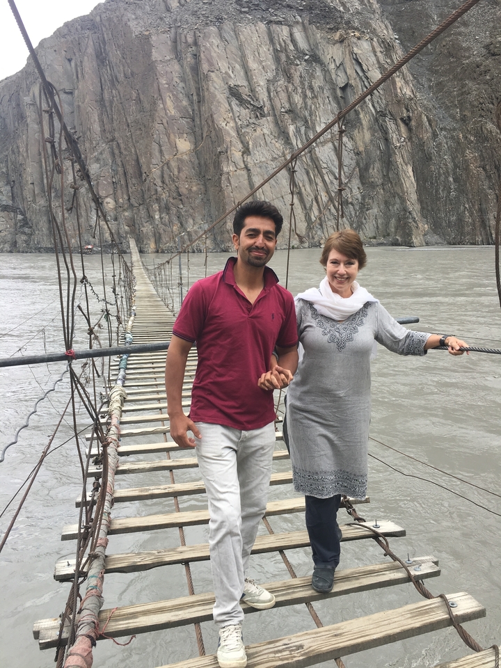 Deux personnes se tenant la main sur un pont suspendu au-dessus d'une rivière.