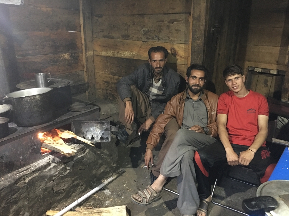 Trois hommes assis à l'intérieur d'une cabane en bois rustique avec un feu.