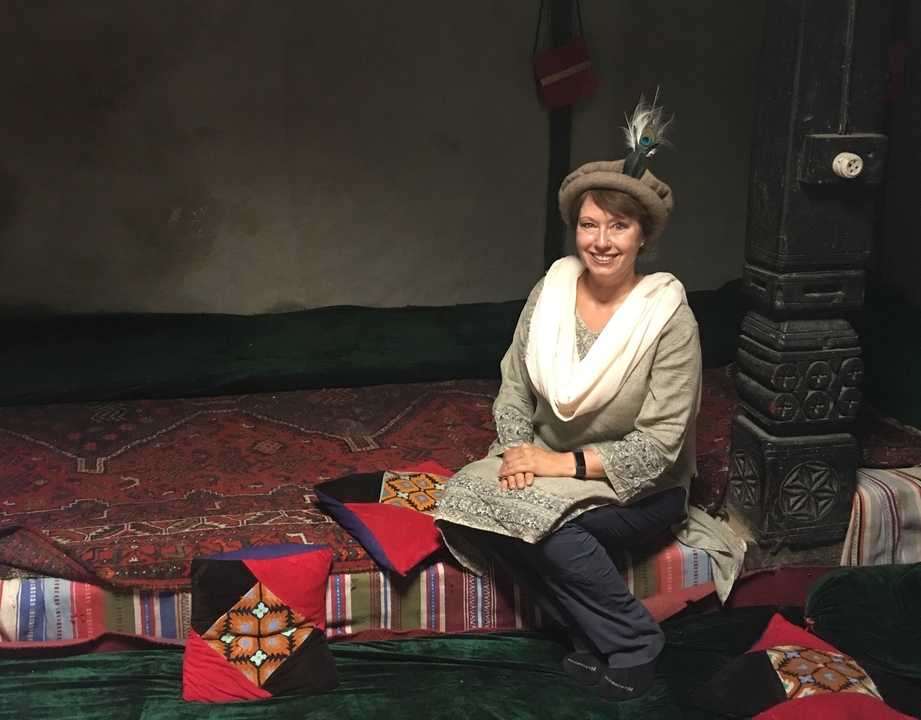 Une femme en tenue traditionnelle assise sur un banc recouvert de tapis.