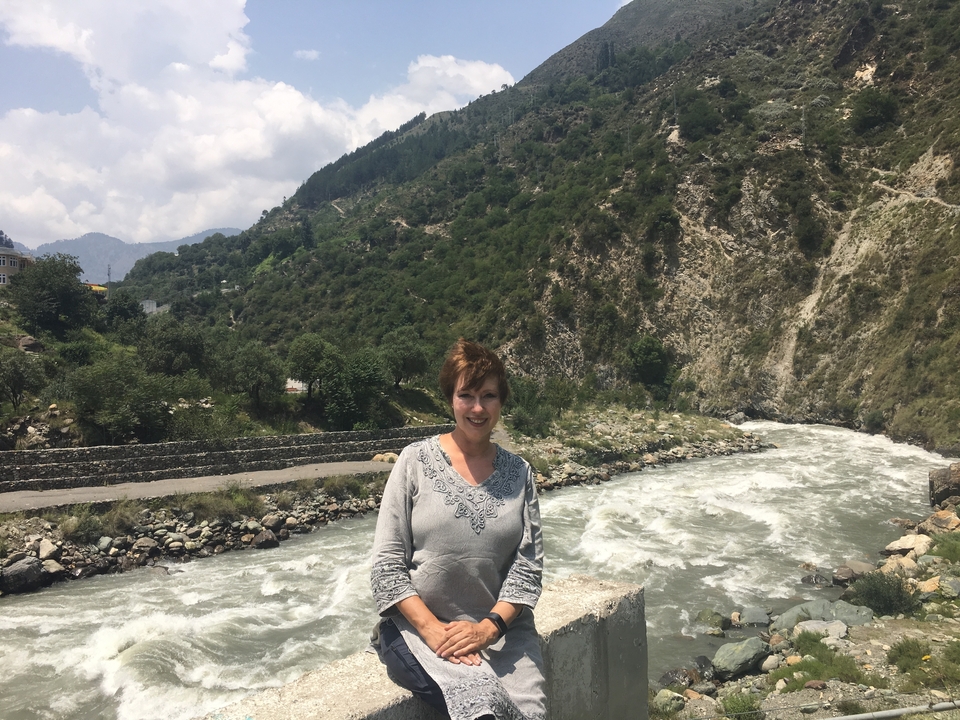 Une femme debout près d'une rivière tumultueuse avec des collines alentour.