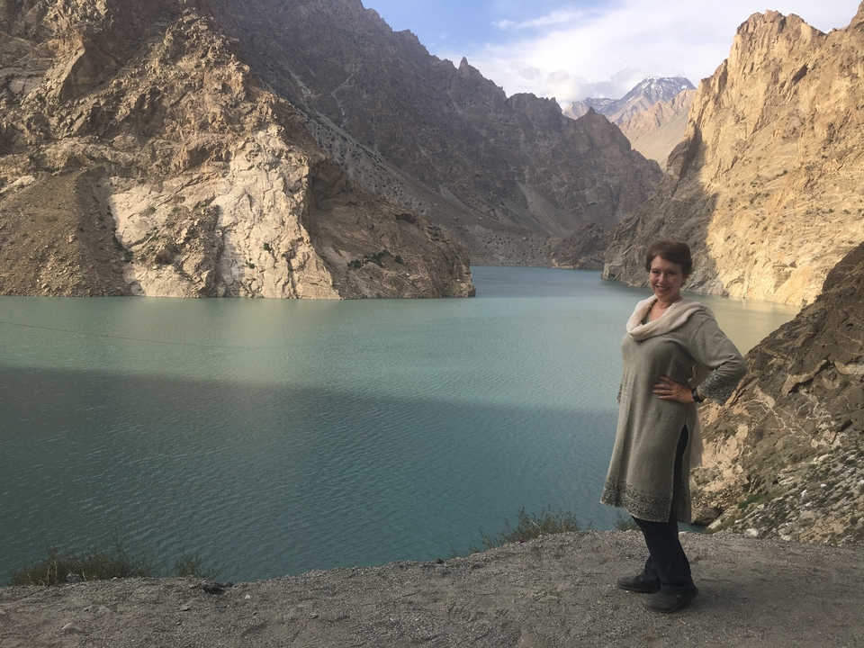 Une femme posant près d'un lac serein avec des falaises rocheuses en arrière-plan.