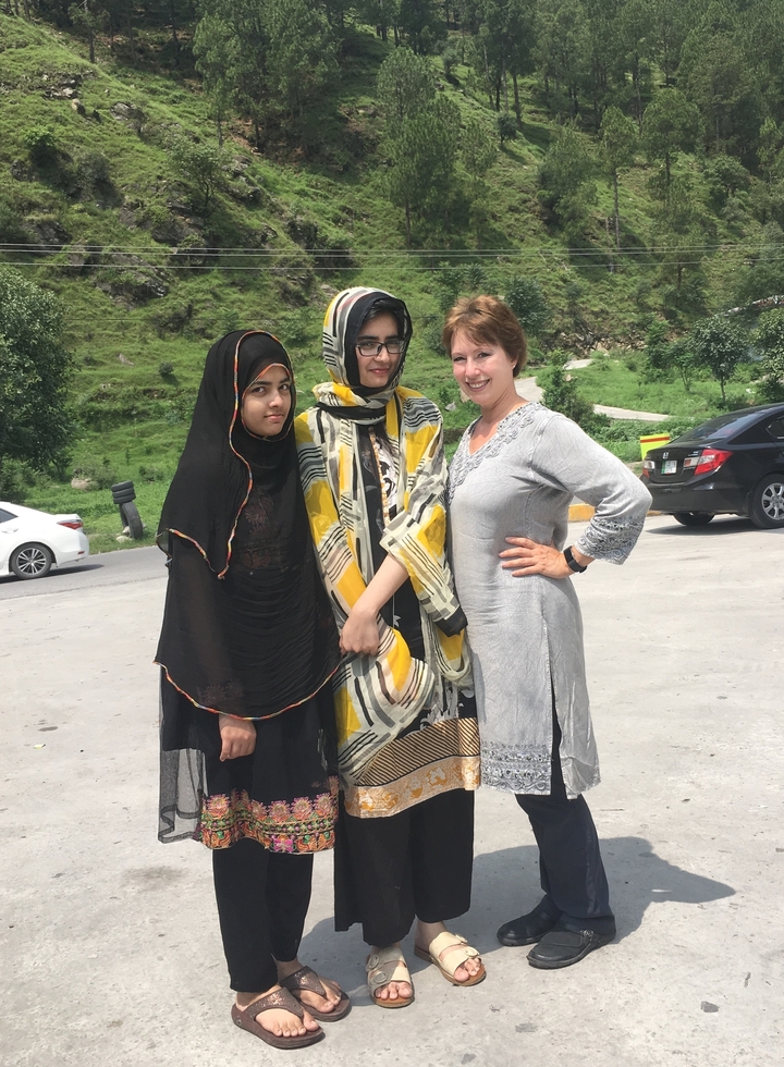 Trois femmes debout dehors avec des arbres et une voiture en arrière-plan.