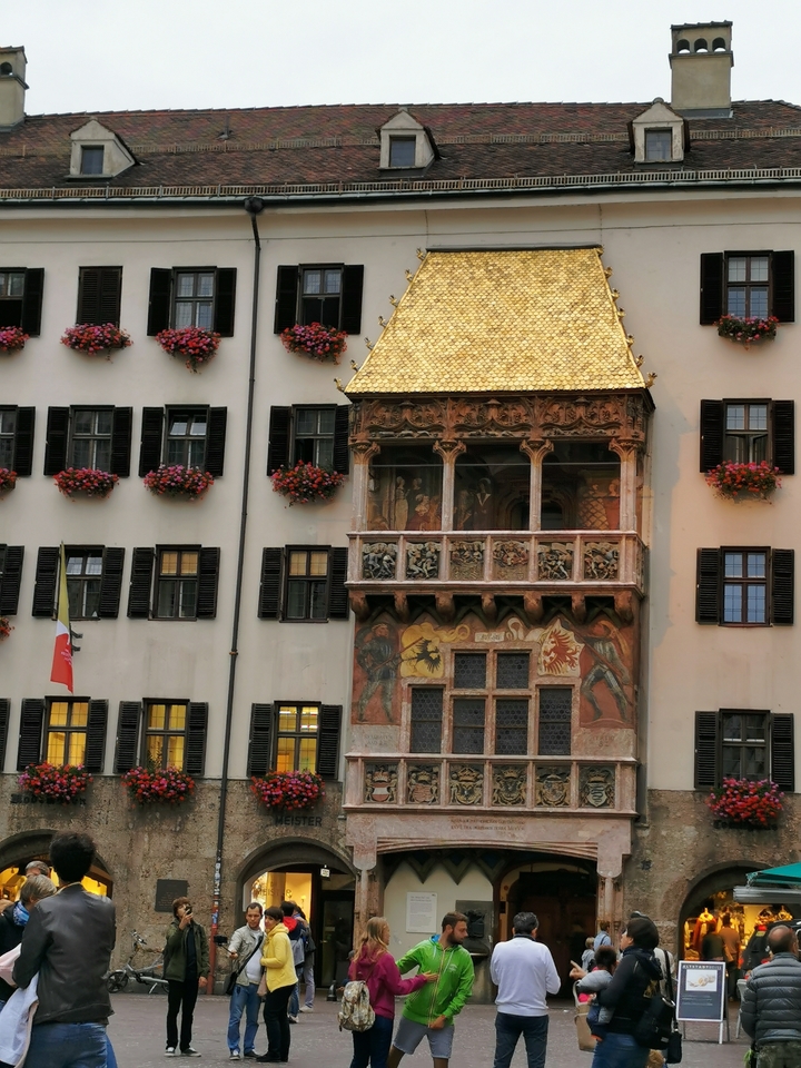 Un bâtiment avec un balcon doré et des fleurs rouges.