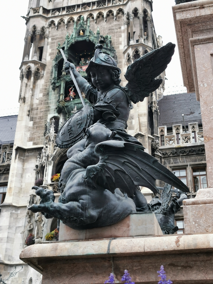 Une statue d'un ange avec un bouclier sur un arrière-plan de bâtiment.
