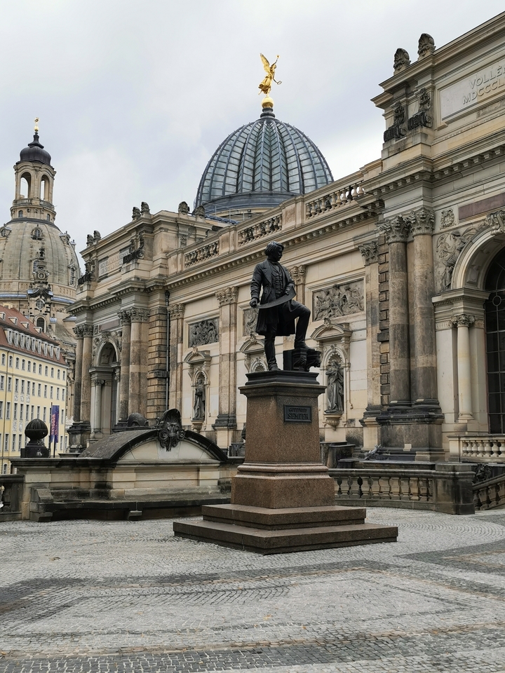 Statue devant une architecture classique ornée.