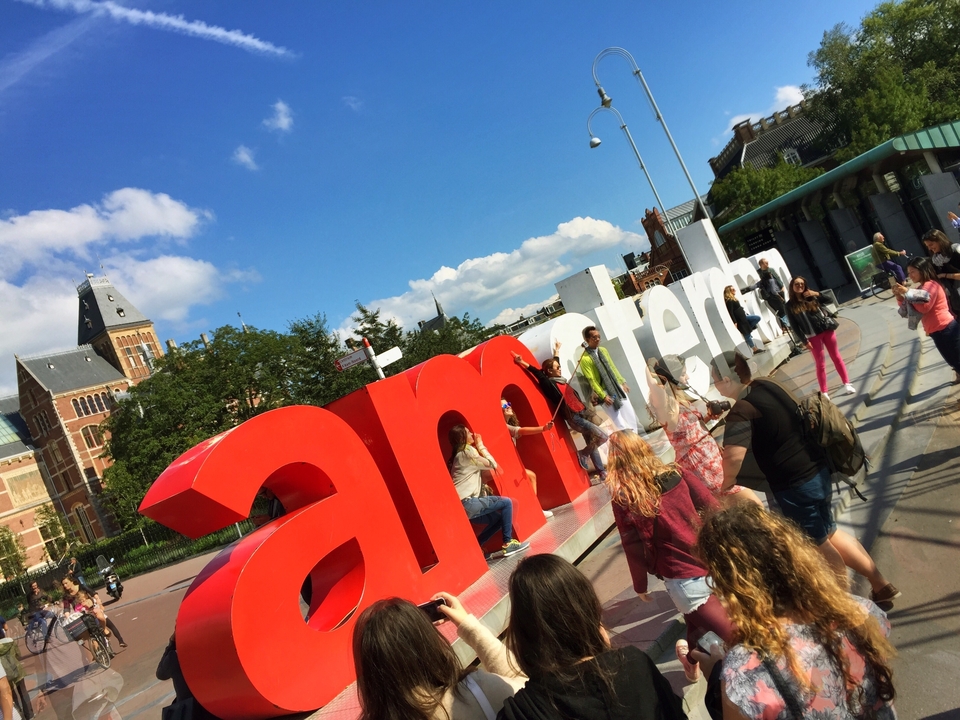 Grand panneau "I Amsterdam" avec des personnes posant devant l'emblème de la ville.