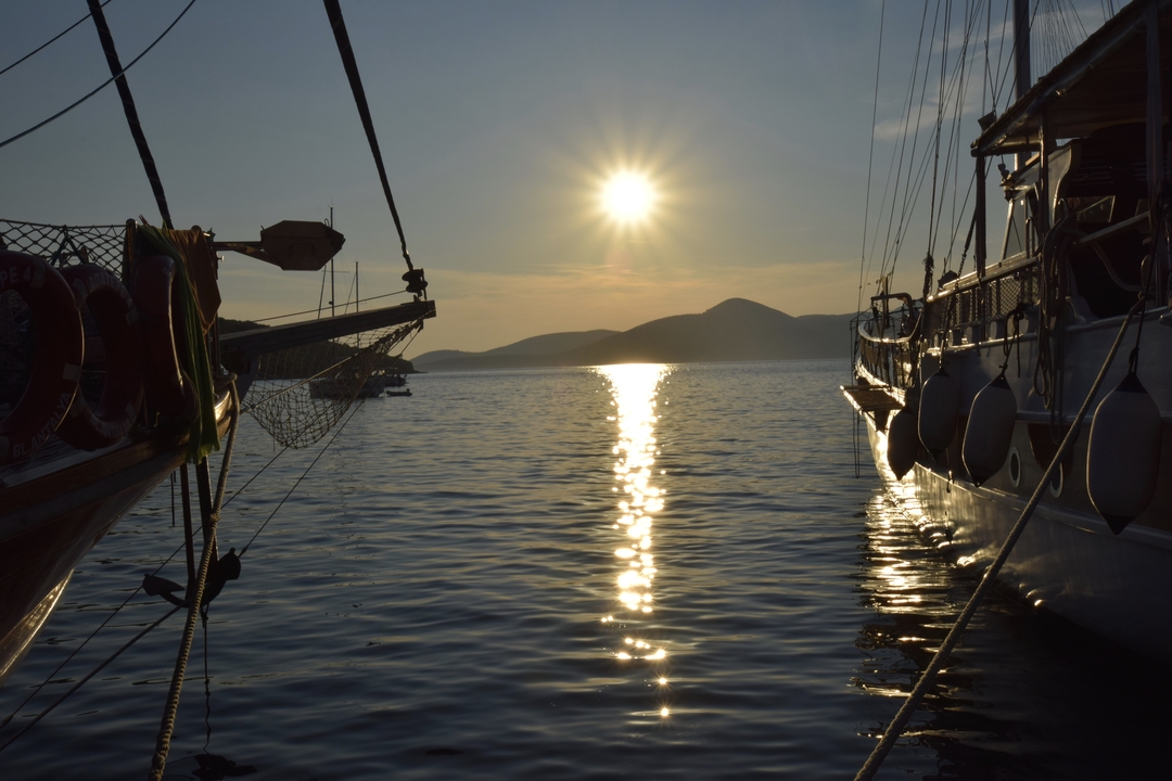 Vue de coucher de soleil entre deux bateaux avec des montagnes au loin.