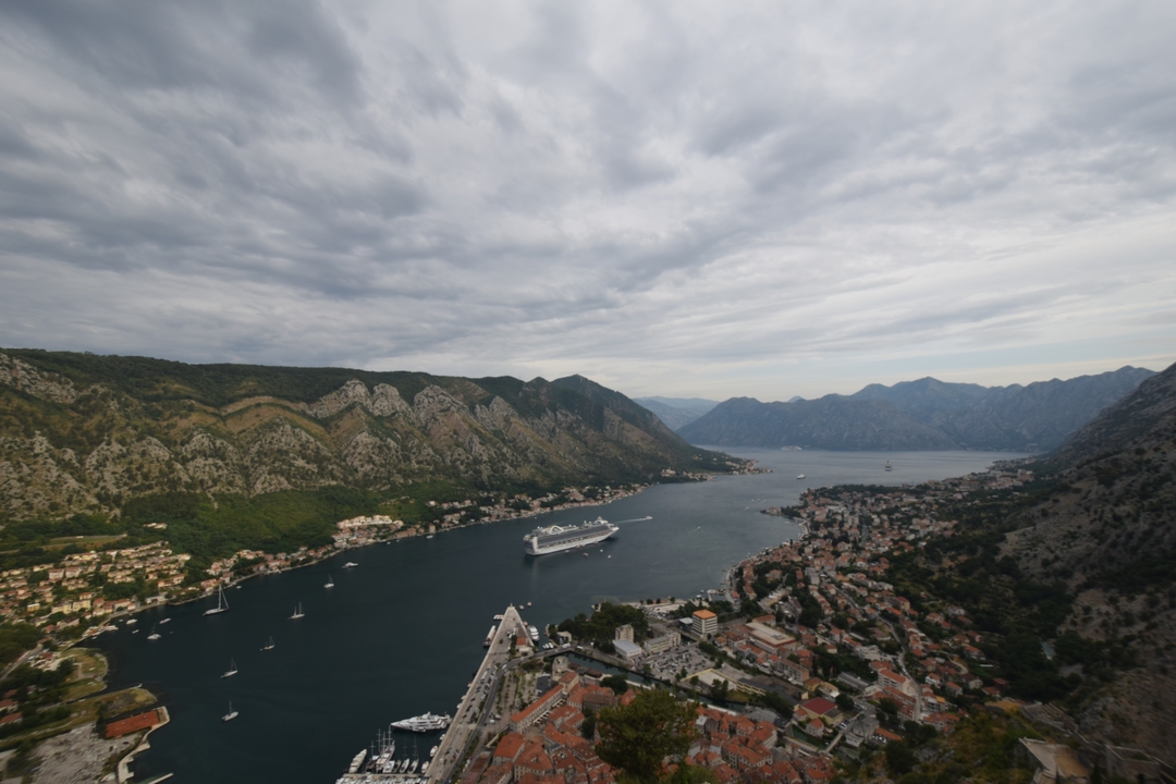Surplombant une baie côtière avec un navire de croisière et un arrière-plan montagneux.