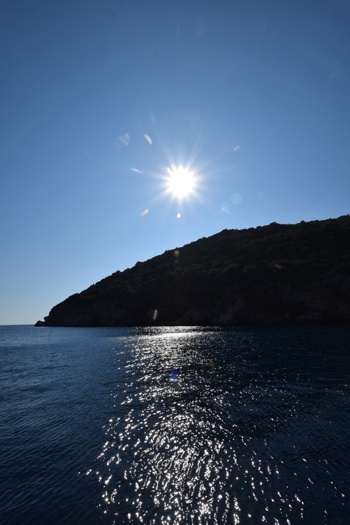 Soleil brillant au-dessus d'une colline, se reflétant sur l'eau.