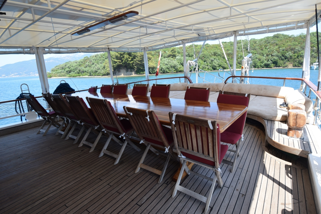 Espace de restauration en plein air sur un bateau avec vue sur la mer et les collines.