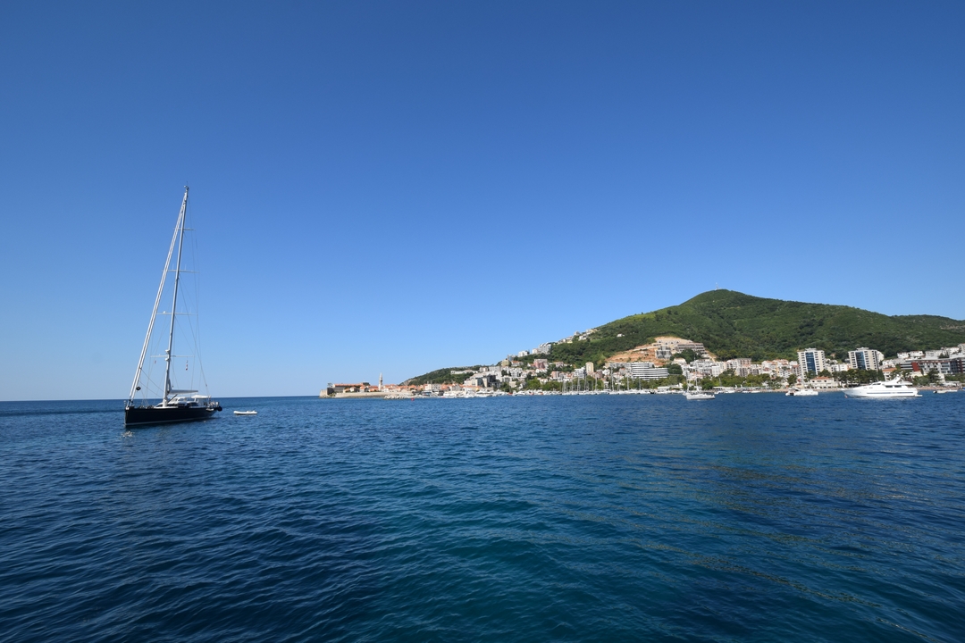 Voilier sur une mer calme avec vue sur une ville à flanc de colline.
