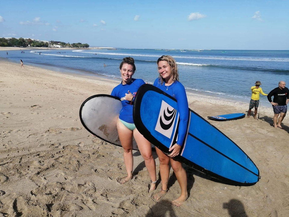 Deux personnes avec des planches de surf sur une plage de sable.