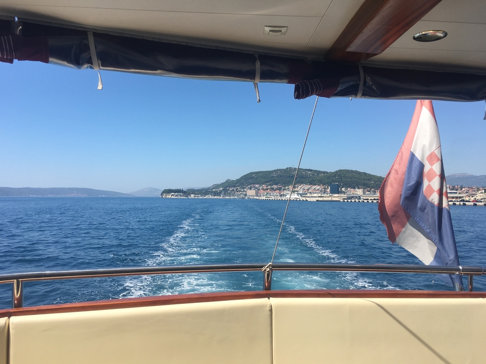 Vue d'une ville côtière depuis un bateau en mouvement, avec un drapeau visible.