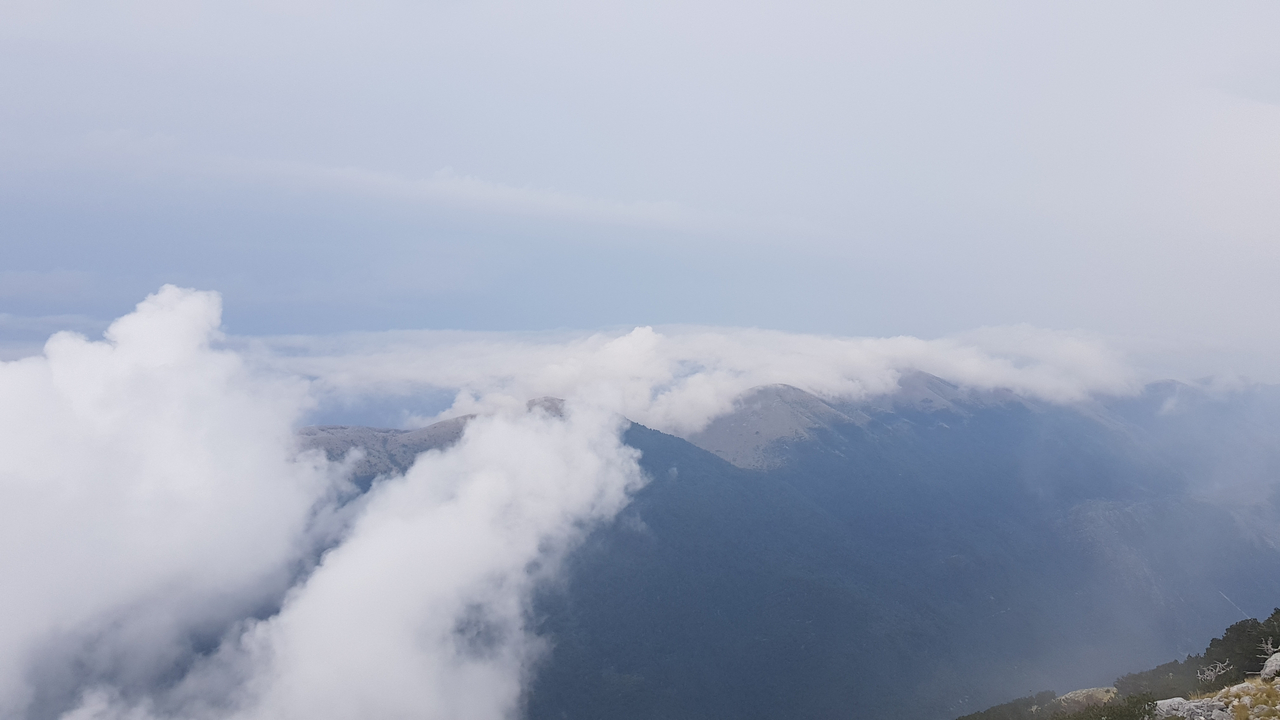 Nuages flottant au-dessus d'une crête montagneuse avec un ciel bleu.