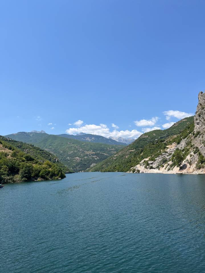 Vaste lac entouré de montagnes vertes sous un ciel bleu dégagé.