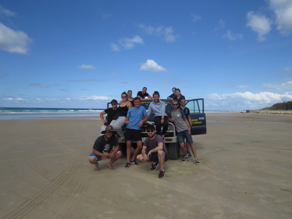 Groupe de personnes posant sur la plage à côté d'un véhicule.