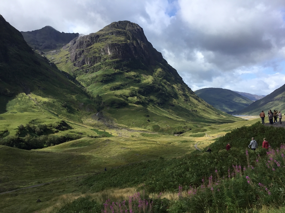 Vallée pittoresque avec montagnes et fleurs, des gens marchant au loin.