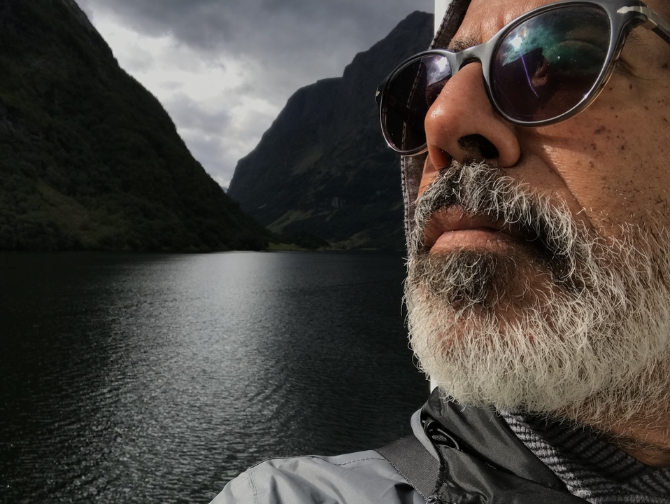 Gros plan du visage d'un homme avec un fjord et des montagnes en arrière-plan.