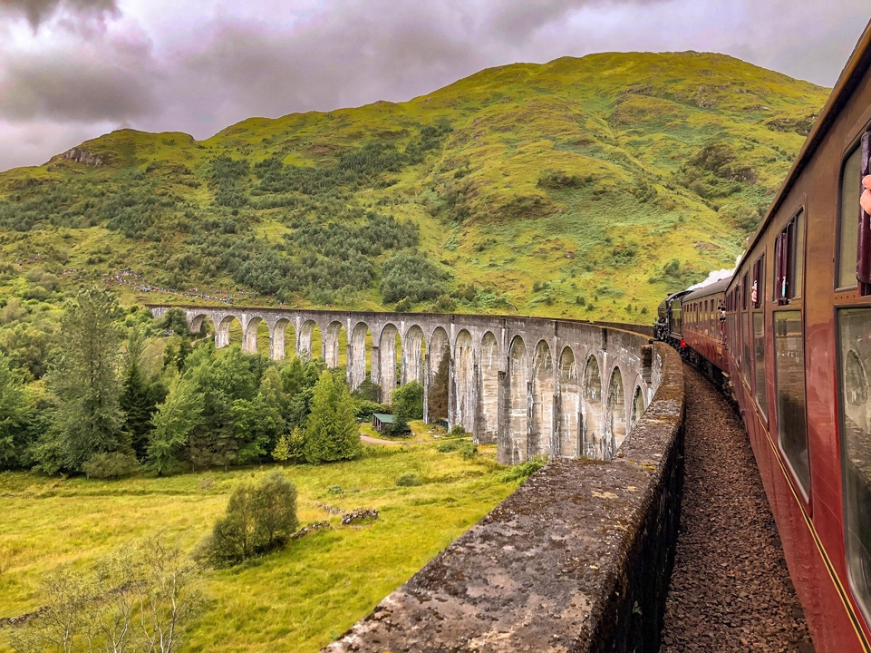 Un train à vapeur historique traversant le célèbre viaduc de Glenfinnan dans une vallée luxuriante.