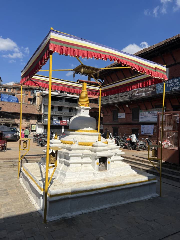 A small white stupa with red roofed structure around it.