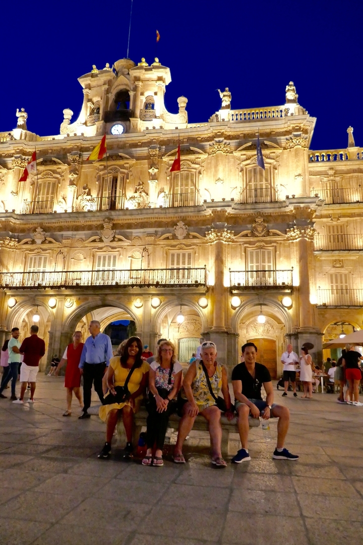 Groupe de personnes assises devant un bâtiment historique illuminé le soir.
