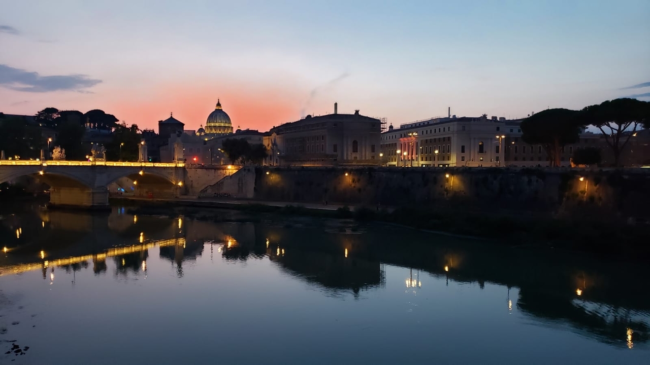 Vue nocturne d'un fleuve avec des bâtiments illuminés, y compris la basilique Saint-Pierre.