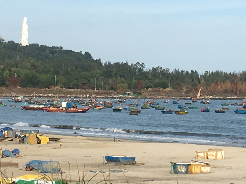 De nombreux bateaux flottant près d'un rivage sablonneux avec des collines au loin.