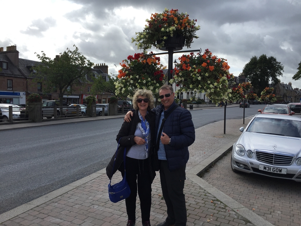 Couple posant sur un trottoir avec des paniers de fleurs suspendus.