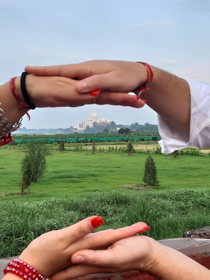 Vue lointaine du Taj Mahal encadrée par des mains.