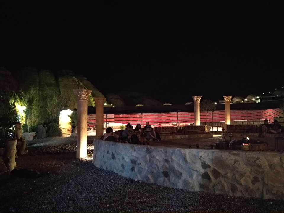 Cour extérieure de nuit avec des sièges en pierre et des structures en forme de tente.