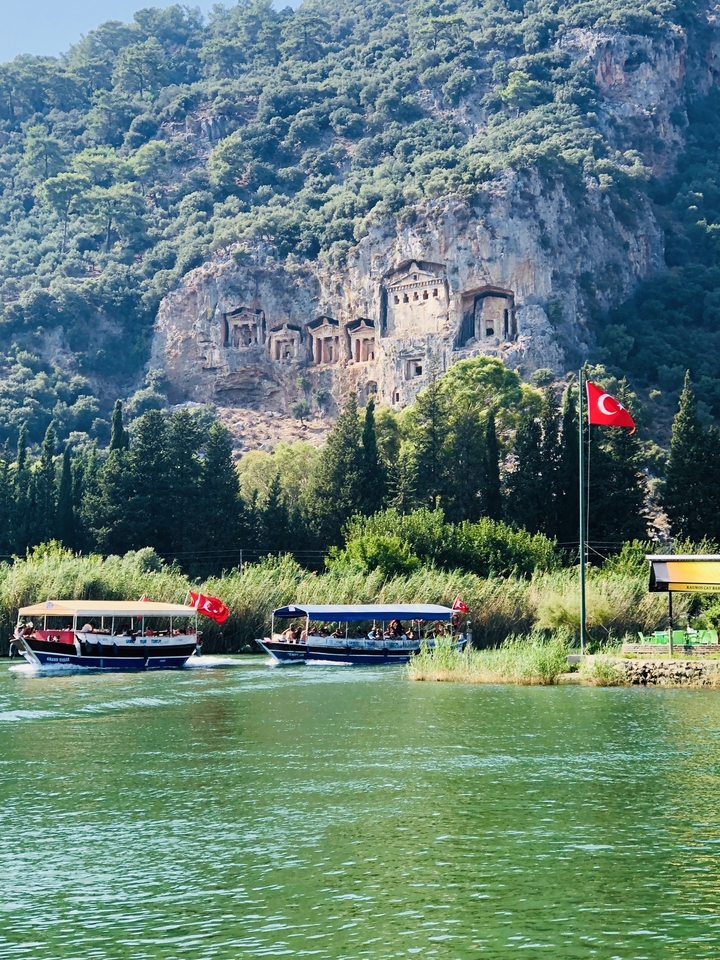 Bateaux sur la rivière près de tombes taillées dans la roche avec des drapeaux turcs