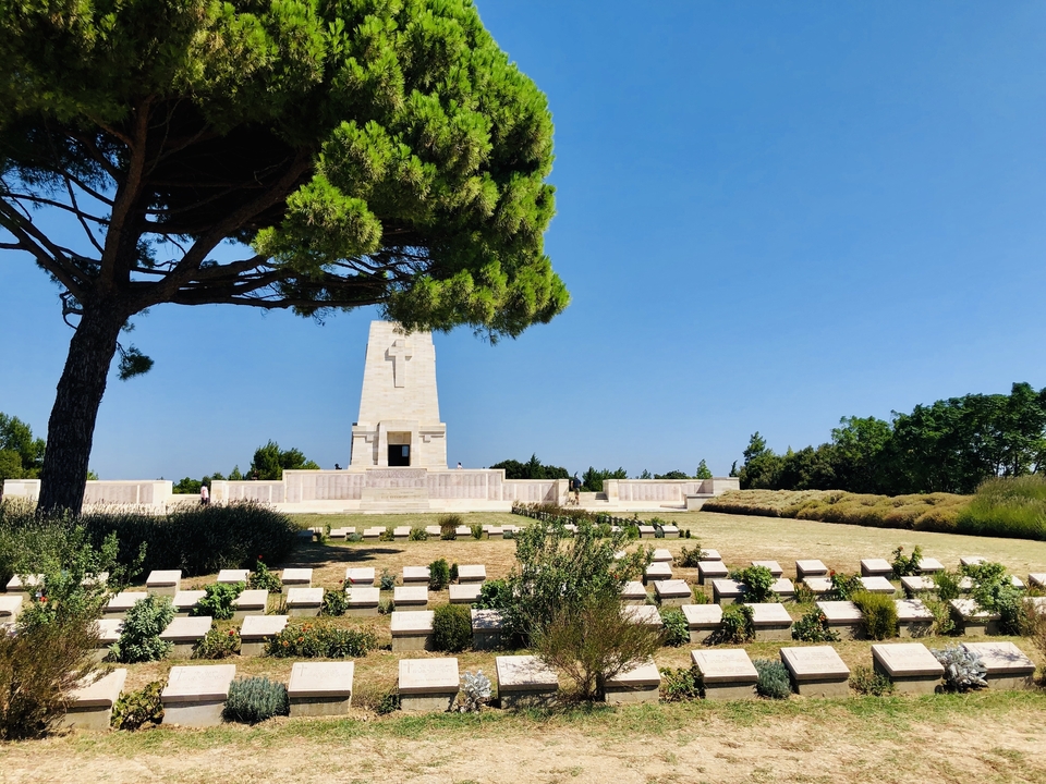 Site commémoratif de guerre avec des pierres tombales et un monument central sous un arbre.