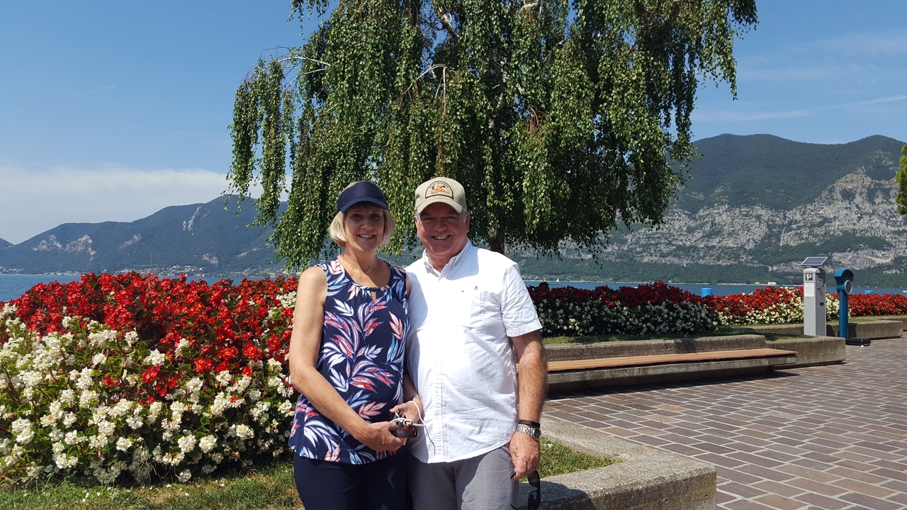 Couple posant à côté d'un arbre avec un paysage de montagne et de lac en arrière-plan.