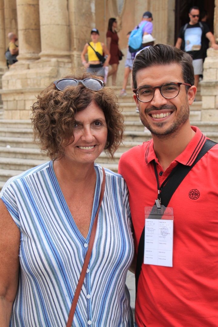 Deux personnes souriantes devant des marches et des bâtiments.