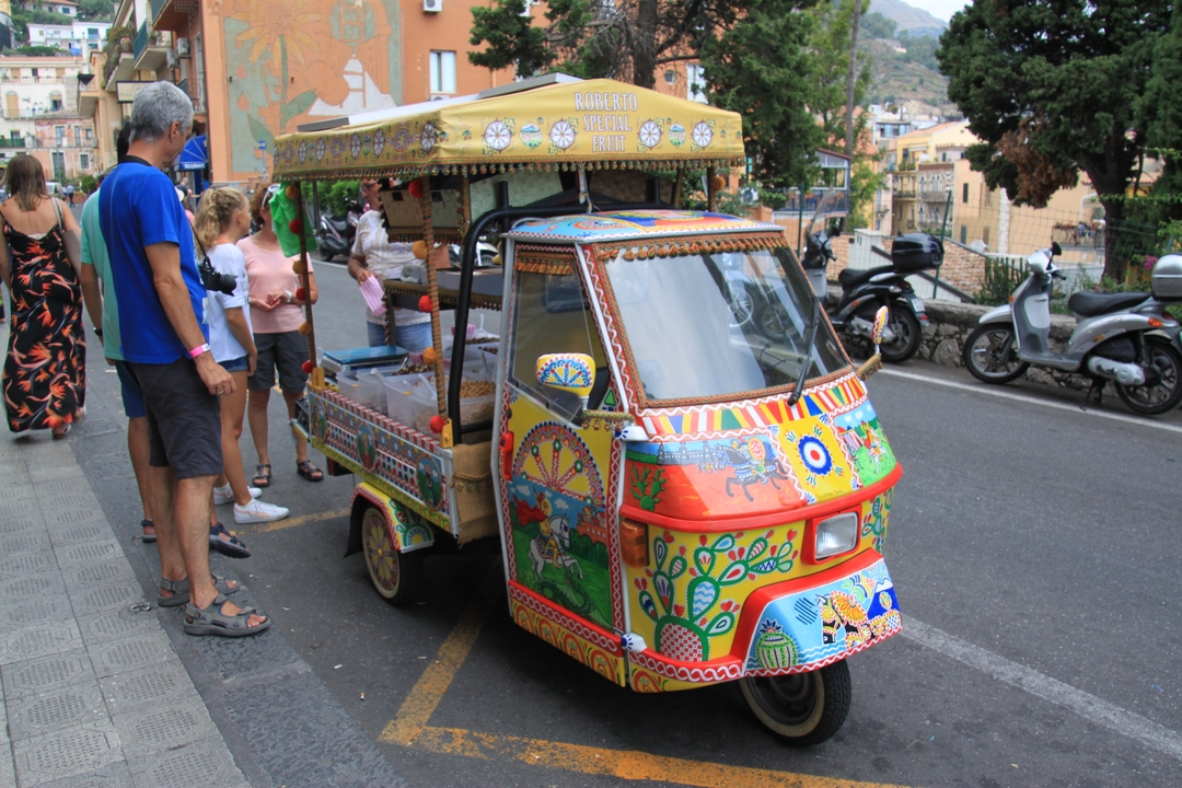 Véhicule coloré décoré sur une rue avec des gens autour.