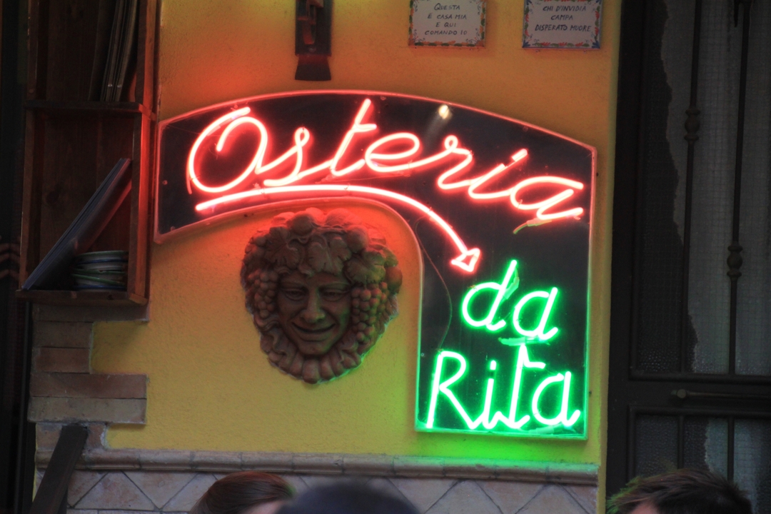 Enseigne au néon d'un restaurant avec une sculpture décorative de visage sur un mur.