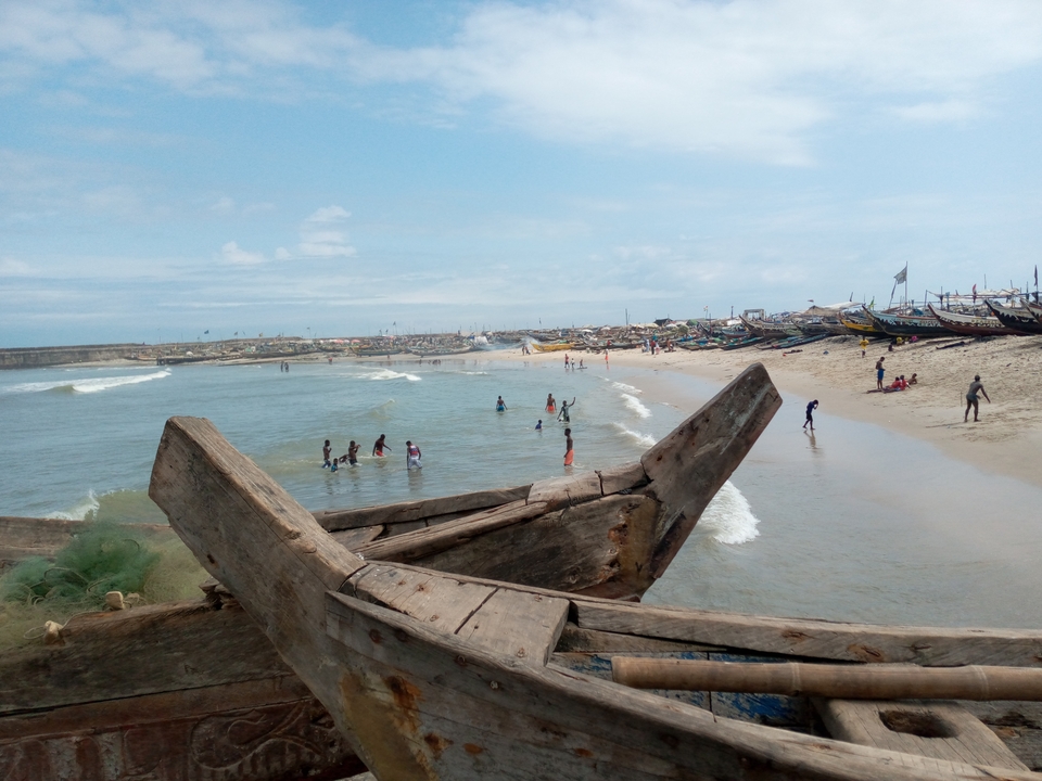 Local beach scene with wooden fishing boats pulled onto sand and swimmers enjoying the surf in Ghana.