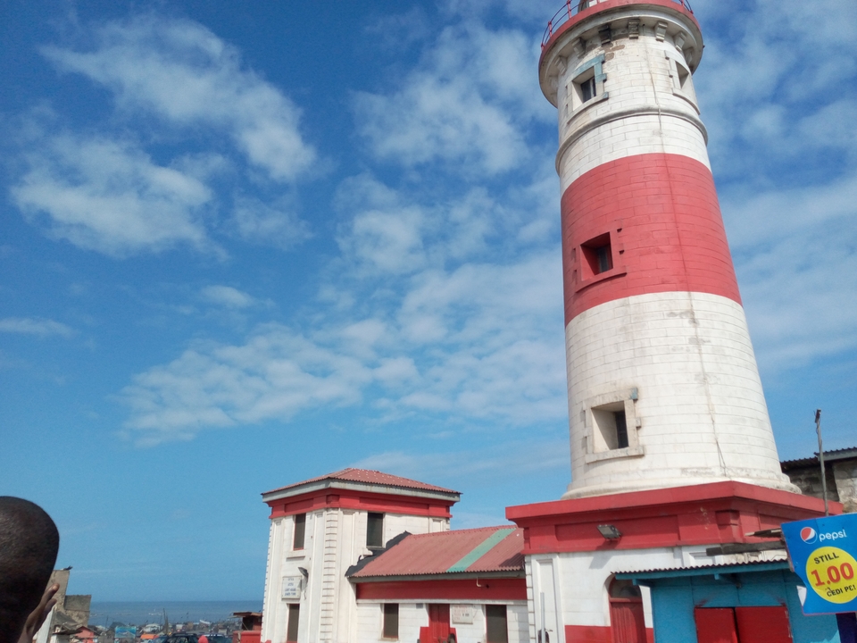 The red-and-white Jamestown lighthouse stands against a bright blue sky dotted with clouds.