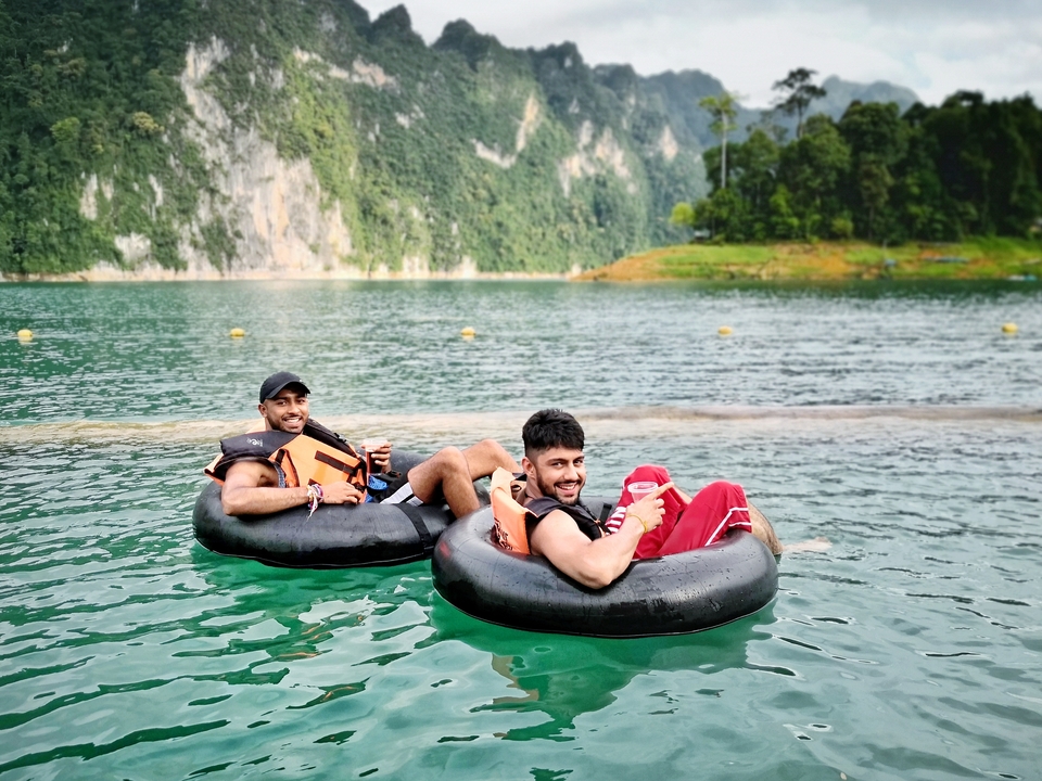 Two people on tubes with drinks in a scenic lake setting.