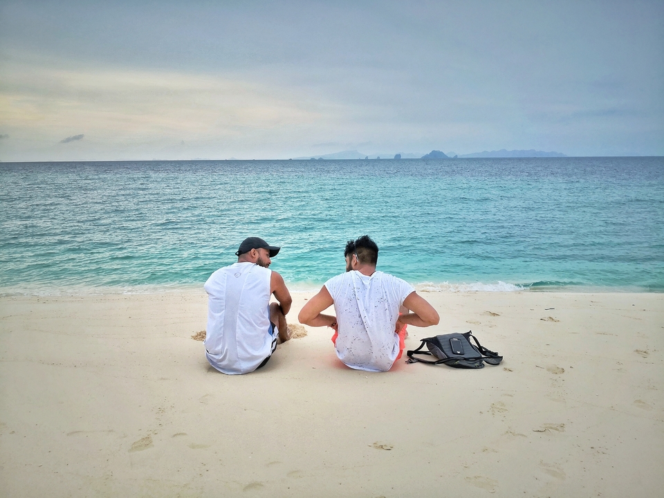 Two people sitting on a beach facing the ocean.