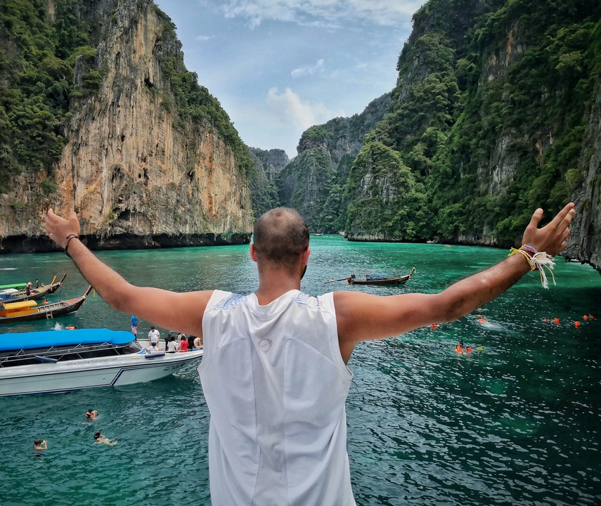Person with arms raised on a boat in a tropical bay with limestone cliffs.