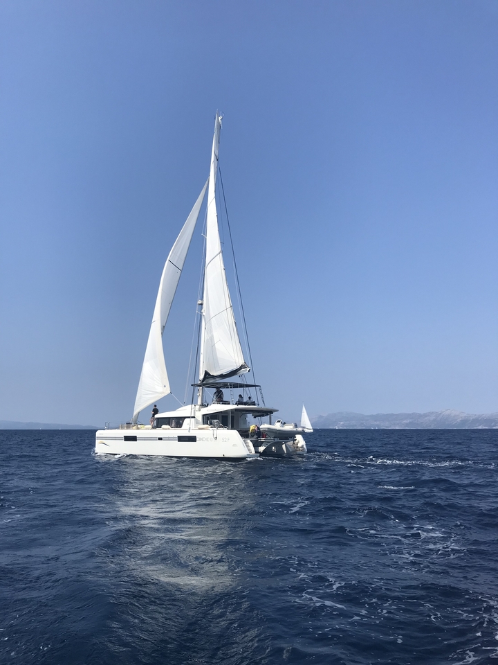Un catamaran naviguant en pleine mer avec des terres lointaines visibles.
