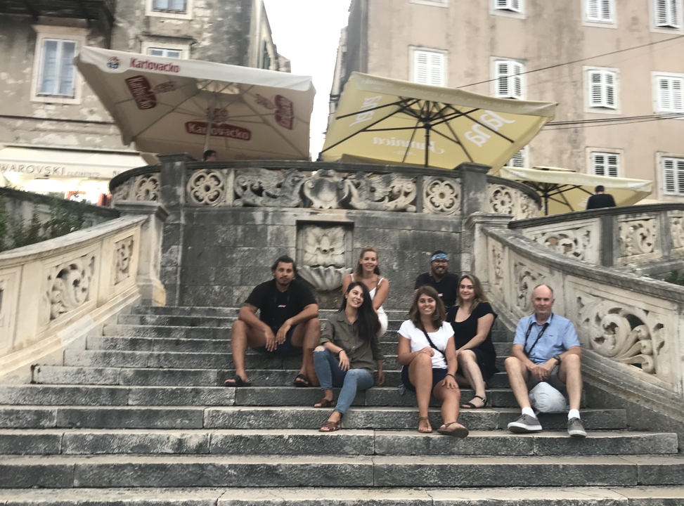 Un groupe de personnes assises sur un escalier sous des parapluies dans un quartier historique.
