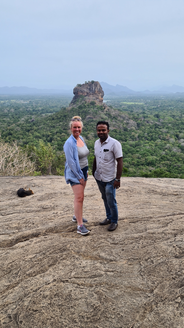Un couple debout sur un rocher avec des collines boisées en arrière-plan.