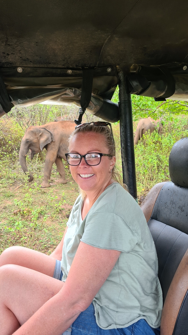 Une personne souriante avec des éléphants en arrière-plan.