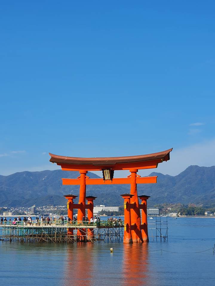 Grand portique torii rouge se dressant dans l'eau avec des montagnes en arrière-plan.
