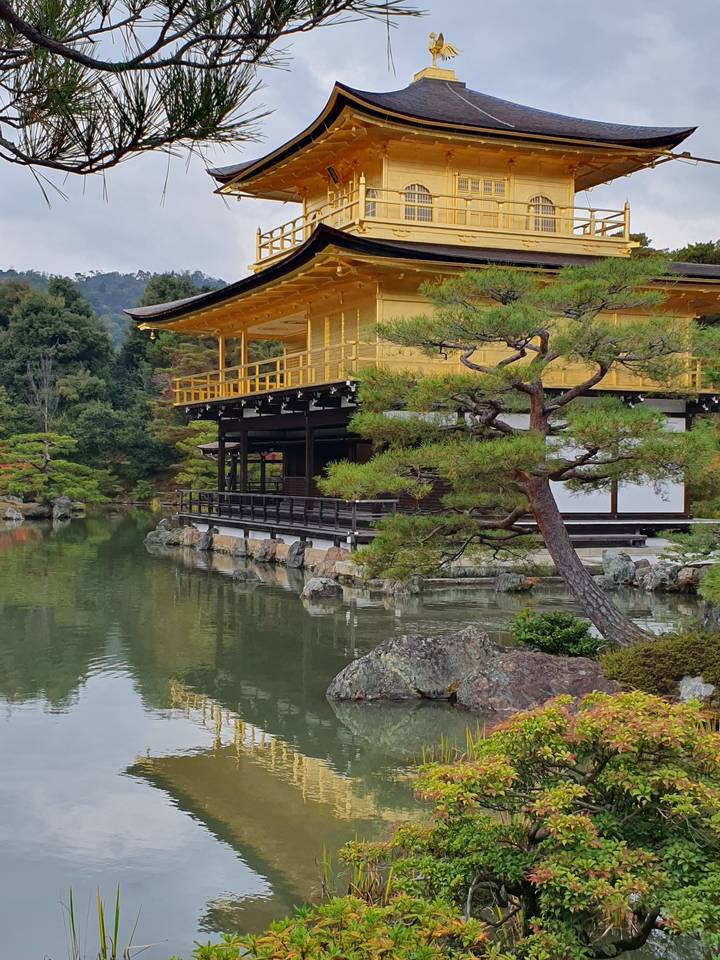 Temple doré reflété dans un étang calme entouré d'arbres.