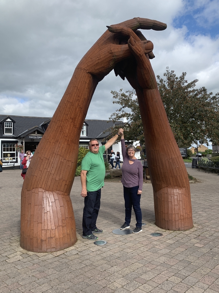 Deux personnes posant sous une sculpture en bois dans un parc.